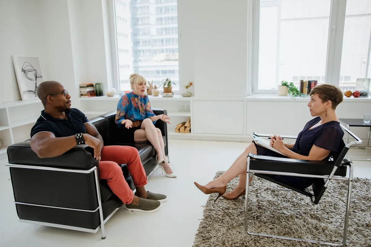 Two clients discussing with a counselor in a bright, modern therapy room.