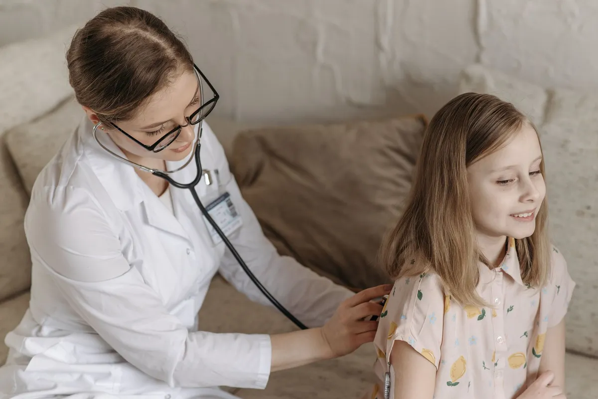 Pediatrician using a stethoscope on a child during a check-up at home.