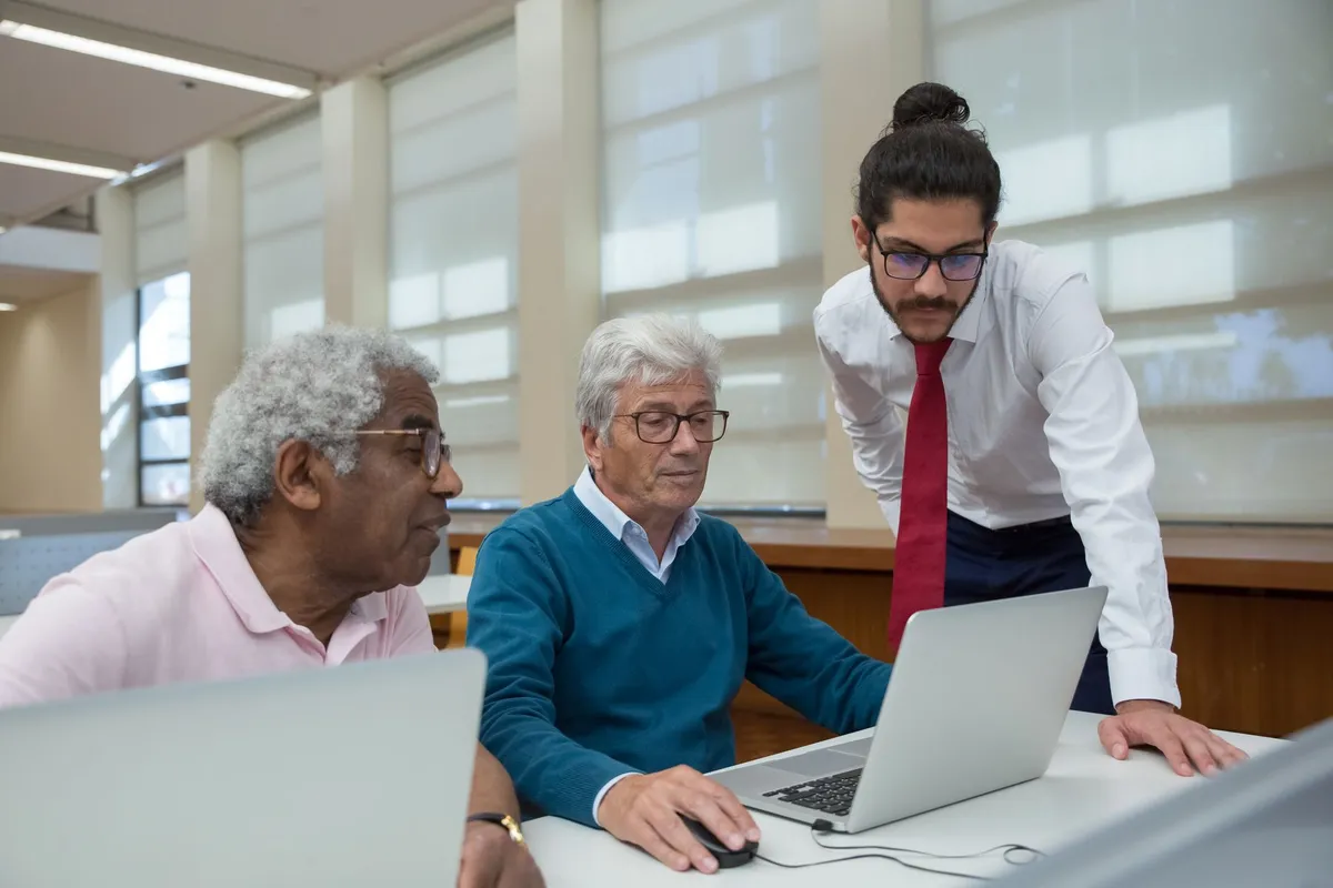 Older adults discussing online safety while using laptops in a library setting.