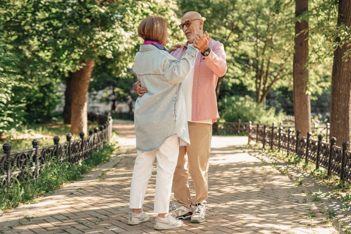 Senior couple dancing together in a park surrounded by greenery.