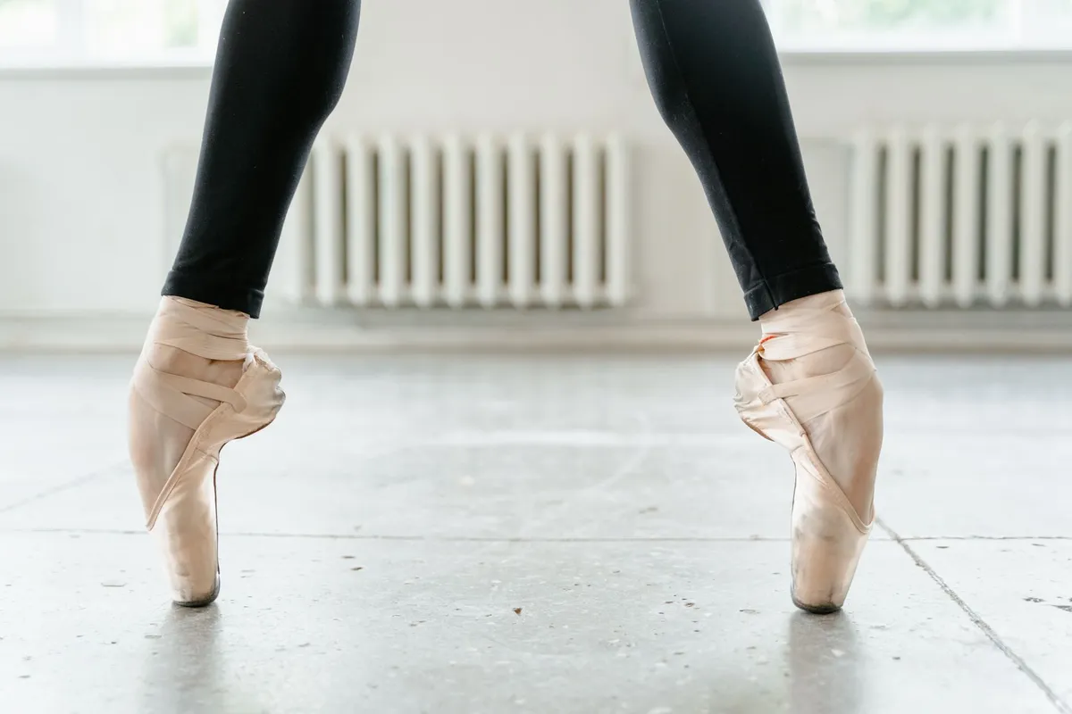 Ballet dancer in pointe shoes standing on toes in a dance studio.