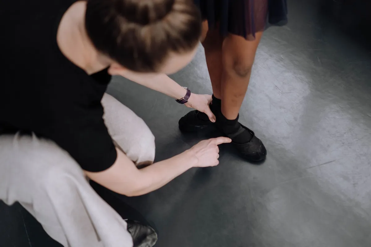 Instructor adjusting a child’s dance shoe for proper fit in a dance studio.