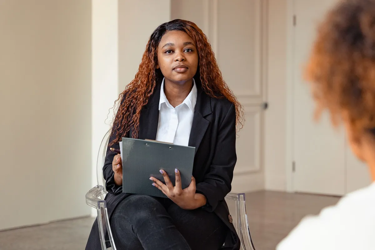 Counselor sitting with a clipboard, engaged in a conversation with a client.