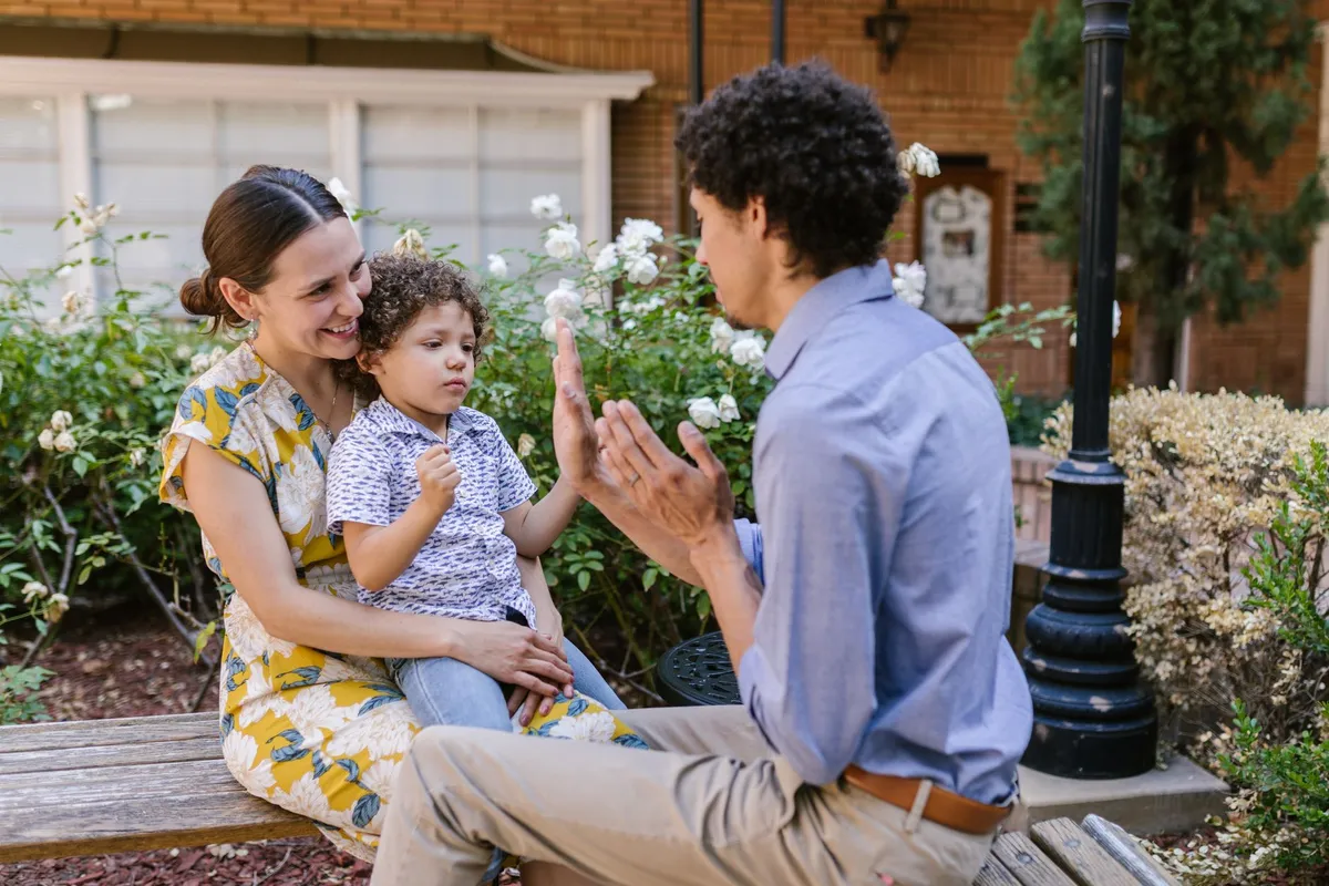 A family using sign language while interacting with a child outdoors.