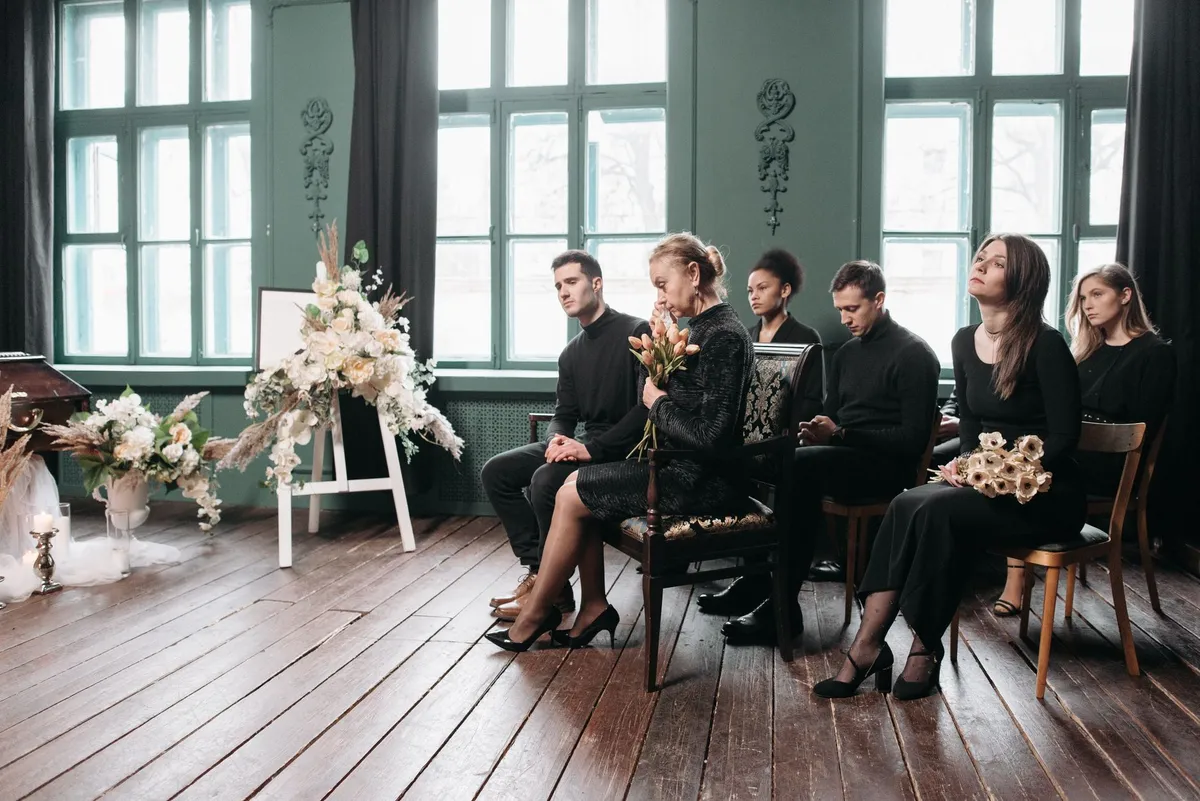 Group of people seated in a somber setting, attending a memorial service.