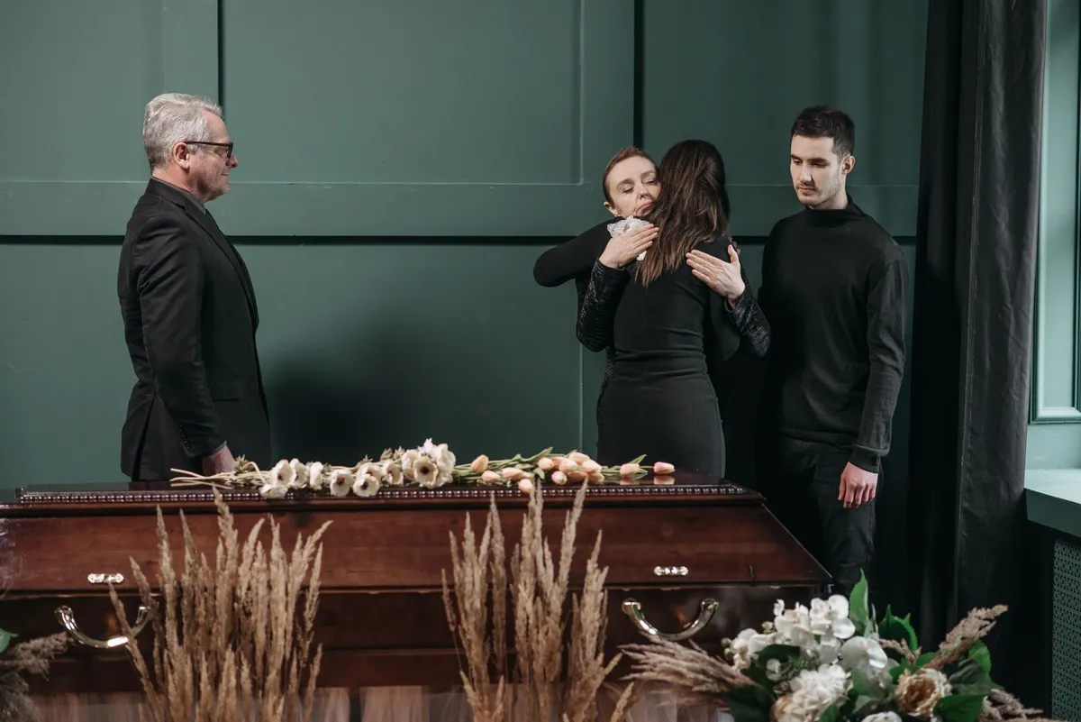 Family members embracing at a funeral service near a casket.