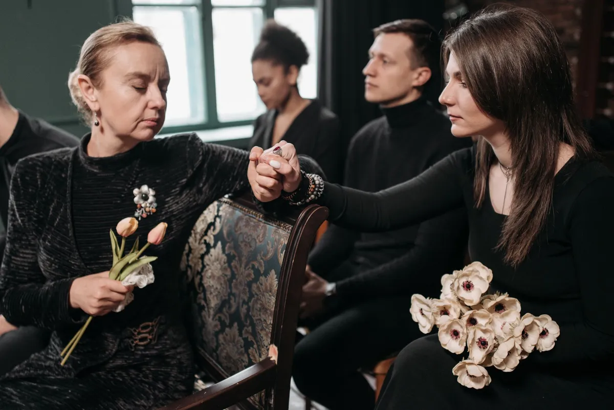 Group of grieving individuals holding hands in a supportive setting.