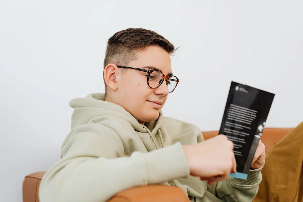 Young person reading a booklet while sitting on a couch.