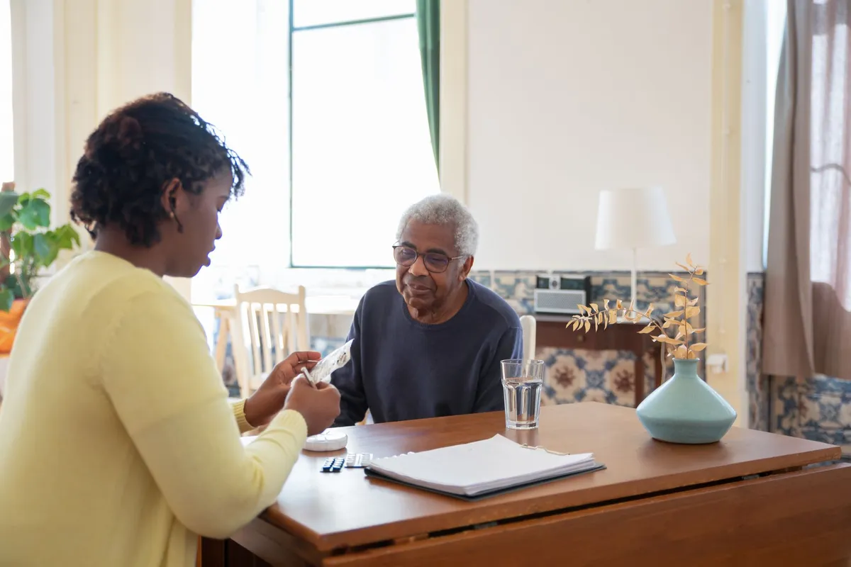 Caregiver assisting an elderly man with a financial document in a home setting.