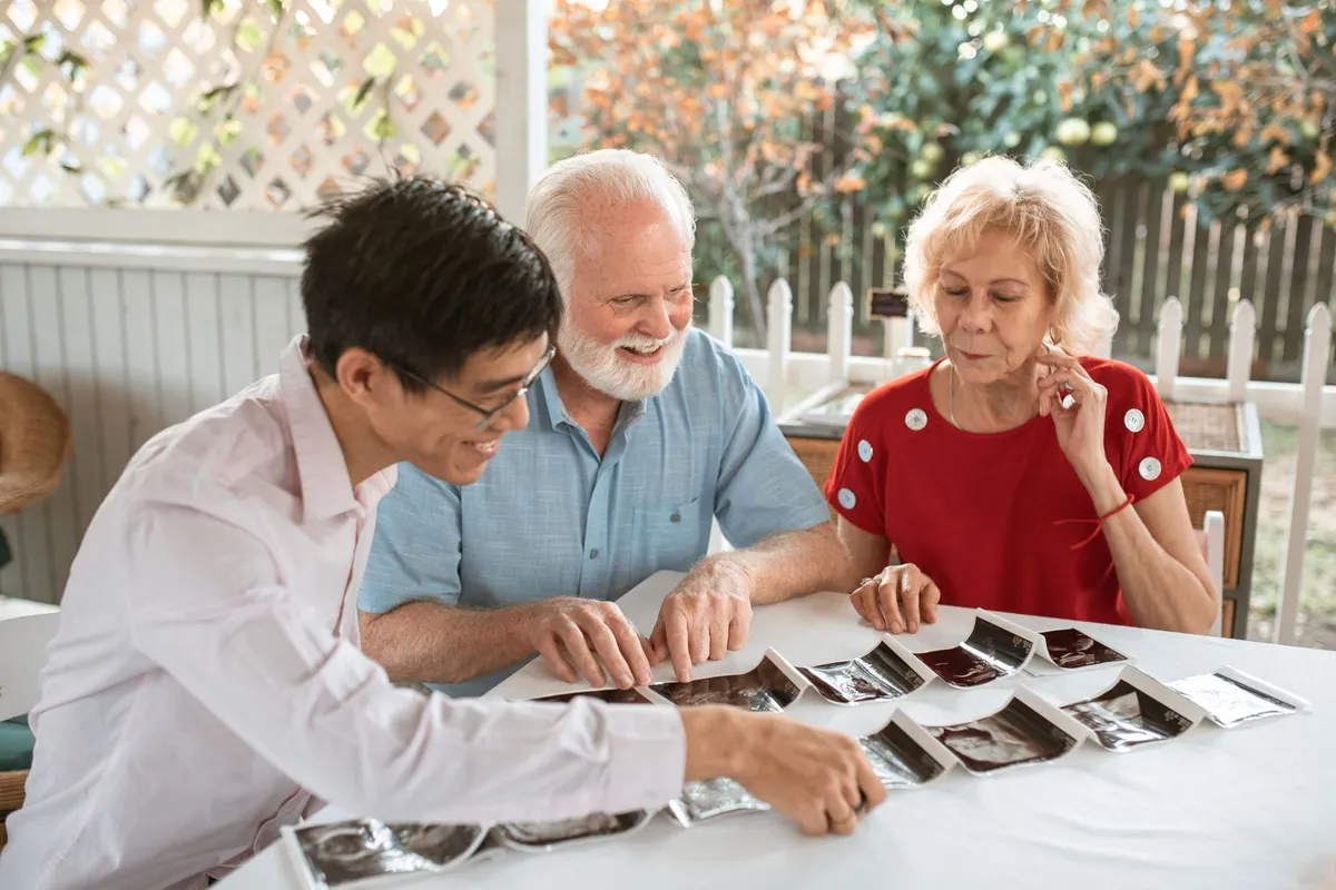 Three people looking at photographs together, discussing memories in a home setting.