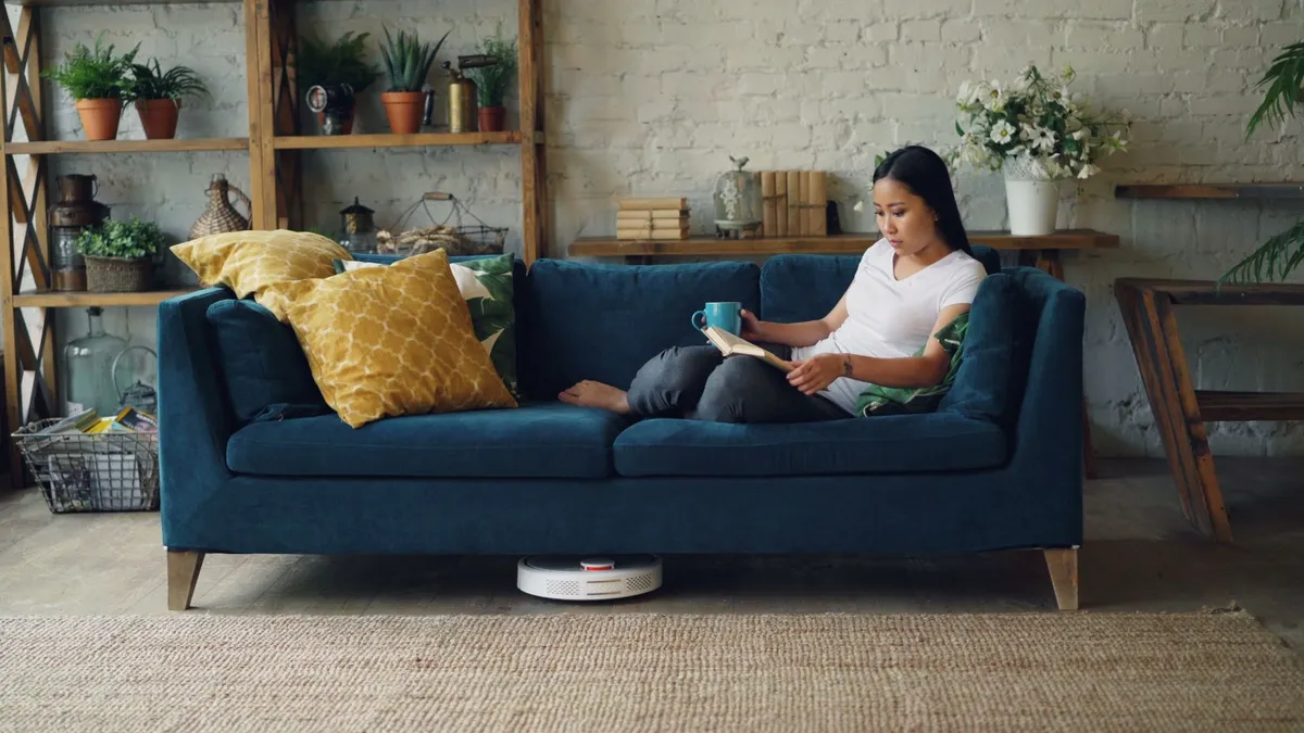 Woman reading a book on a couch with plants in a cozy living room setting.